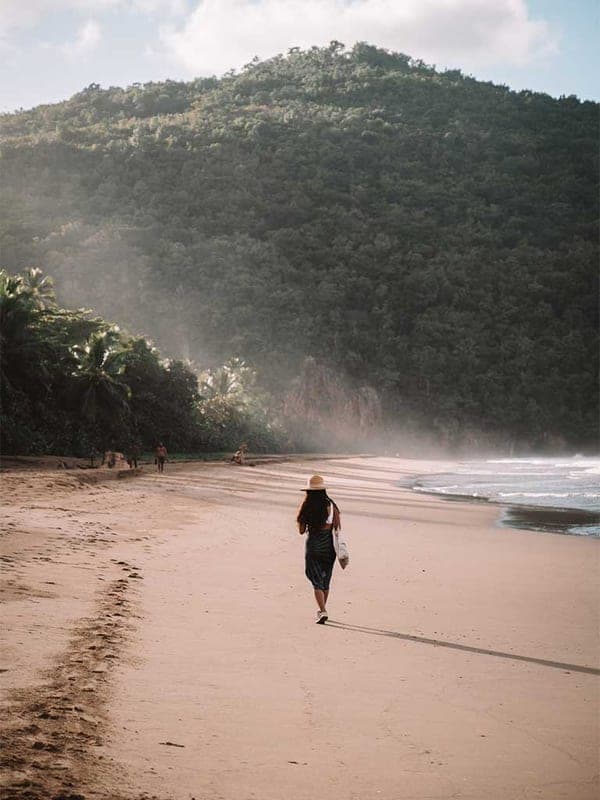 A visitor walking the sand at El Valle beach, jungle mountains rising behind