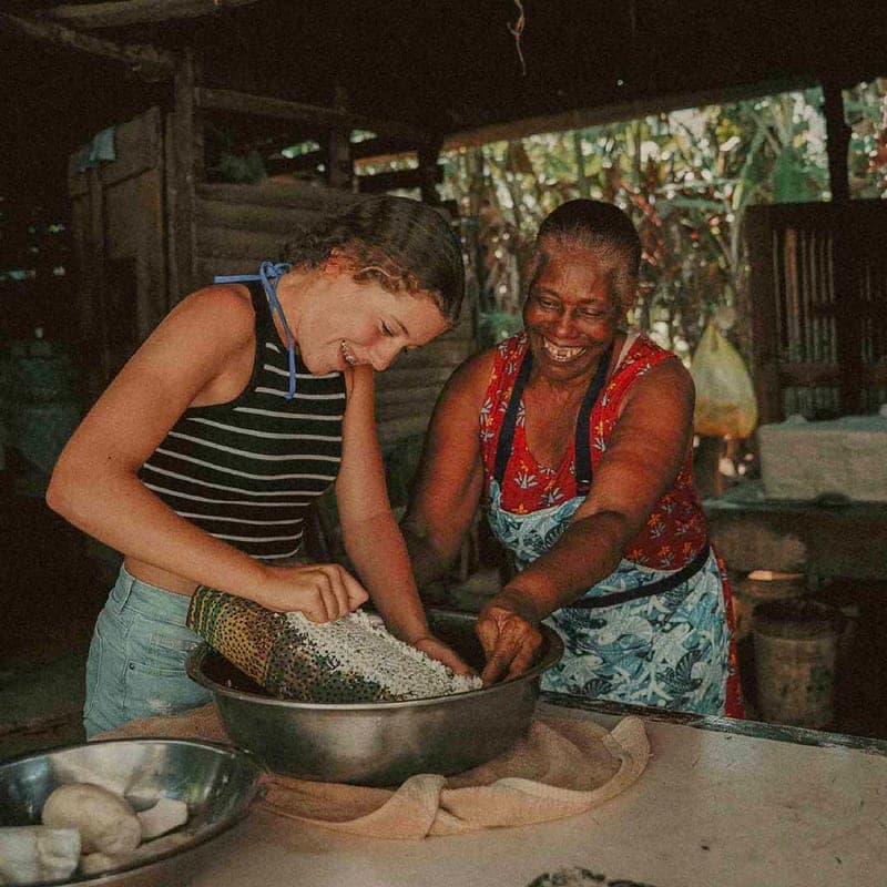A visitor and a local woman cooking together at a table in El Valle